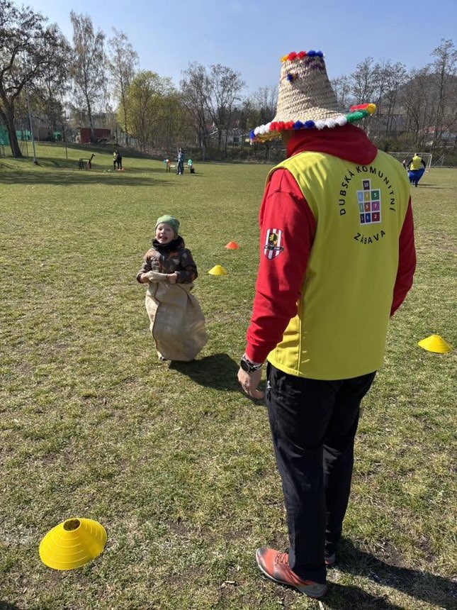 Dítě v pytlovém závodě a dobrovolník v týmové vestě na hřišti